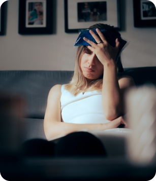 Woman sitting on a couch with a cold pack on her forehead, appearing distressed, representing post-concussion care and neurological support at Apex Chiropractic & Wellness Center.