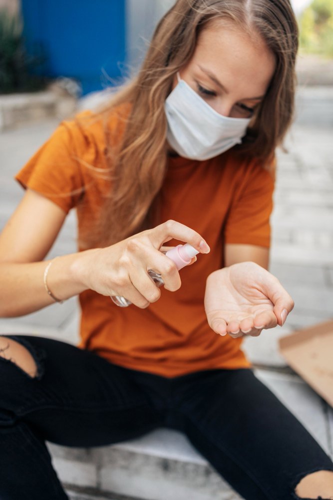 Woman in a mask applying hand sanitizer to her palm, emphasizing hygiene practices relevant to health and wellness, particularly for Lyme disease prevention at Apex Chiropractic & Wellness Center.