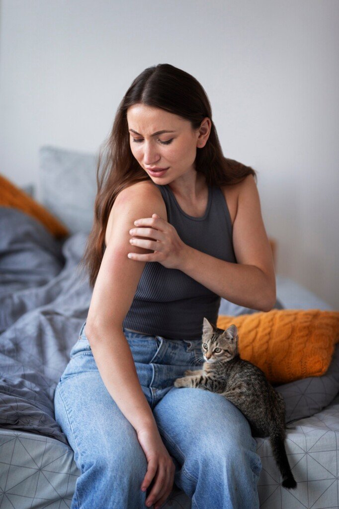 Woman with a rash on her arm, looking concerned, seated on a bed with a kitten beside her, illustrating symptoms relevant to Lyme disease and the importance of early detection.